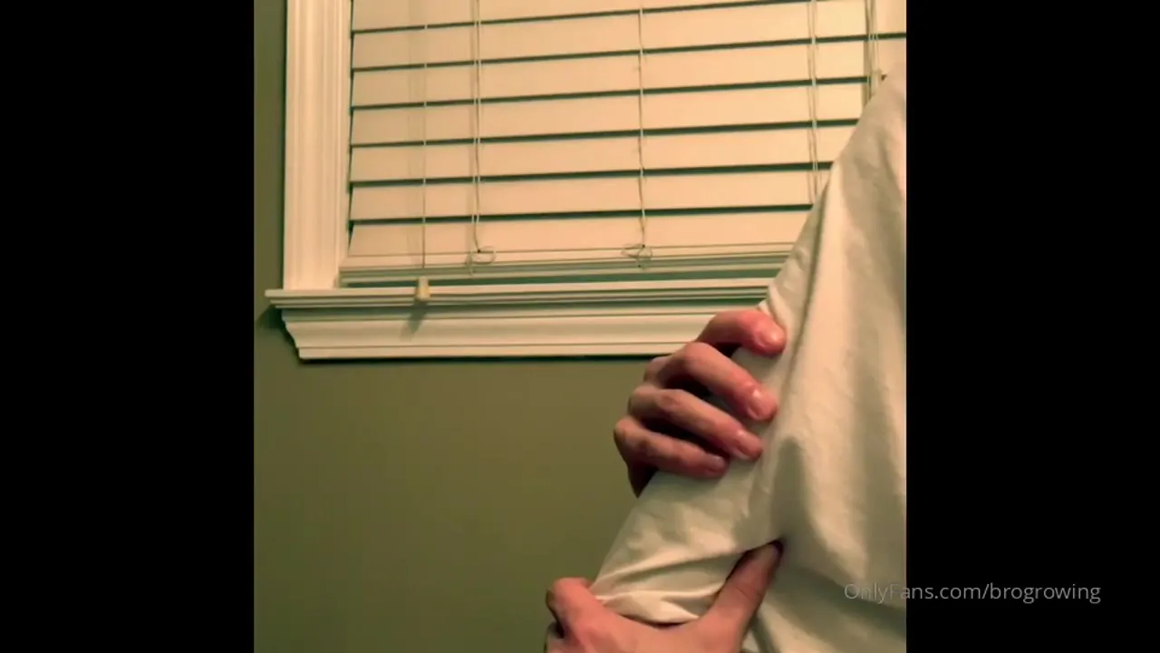 In his white tee by the blinds, Brogrowing frees his soft uncut cock