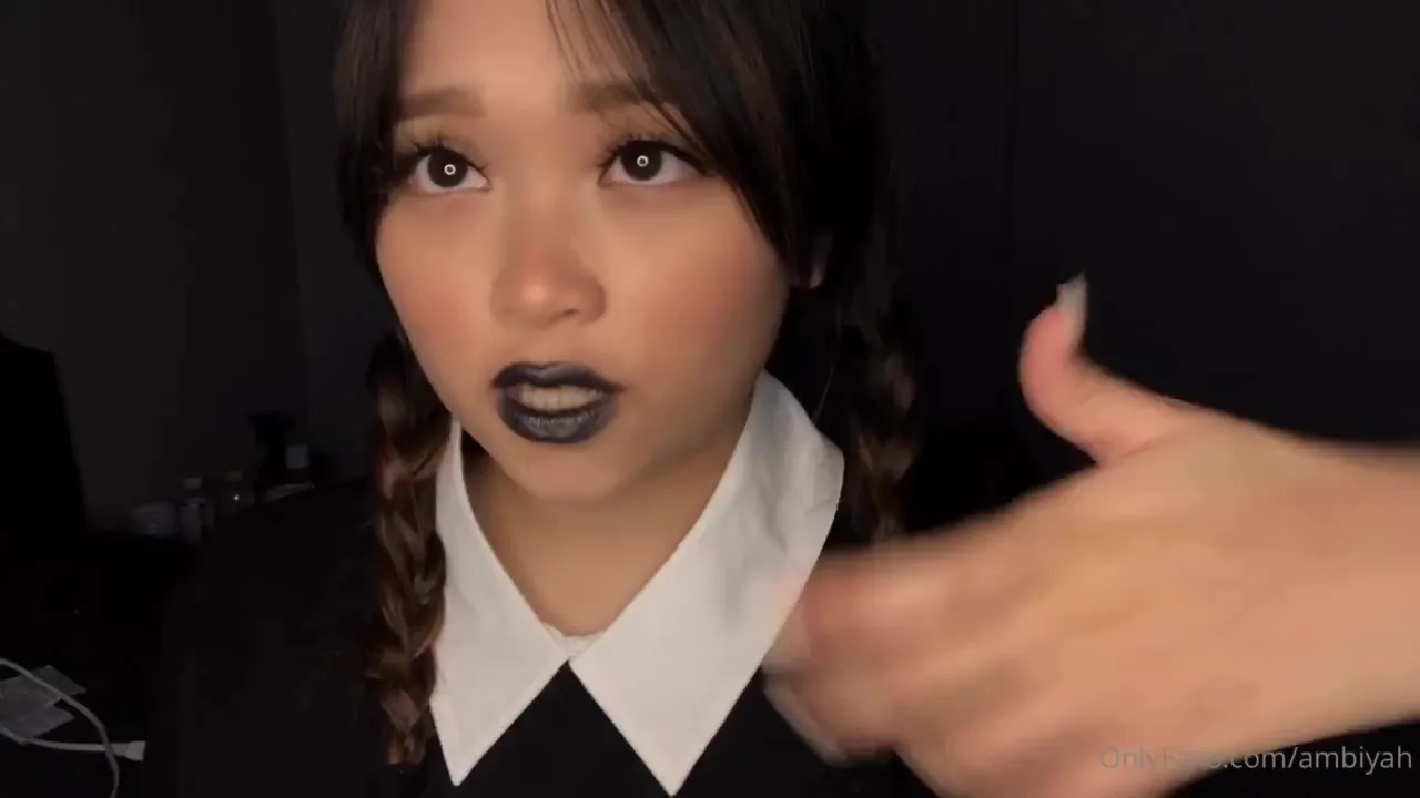 Mae in a schoolgirl outfit, dark lipstick and braids, eager and filthy