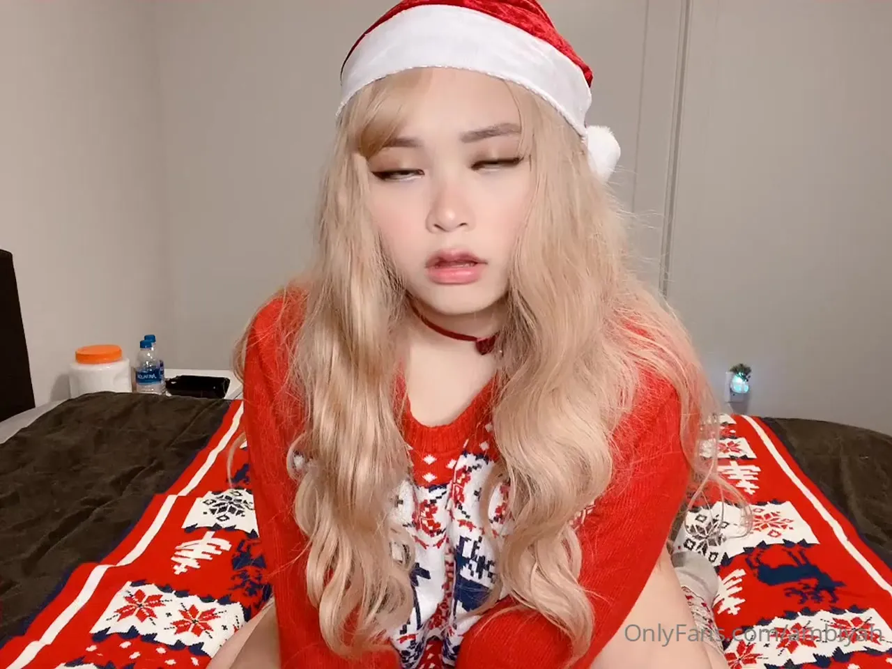 Mae in a Santa hat, sitting on the bed in a red Christmas sweater