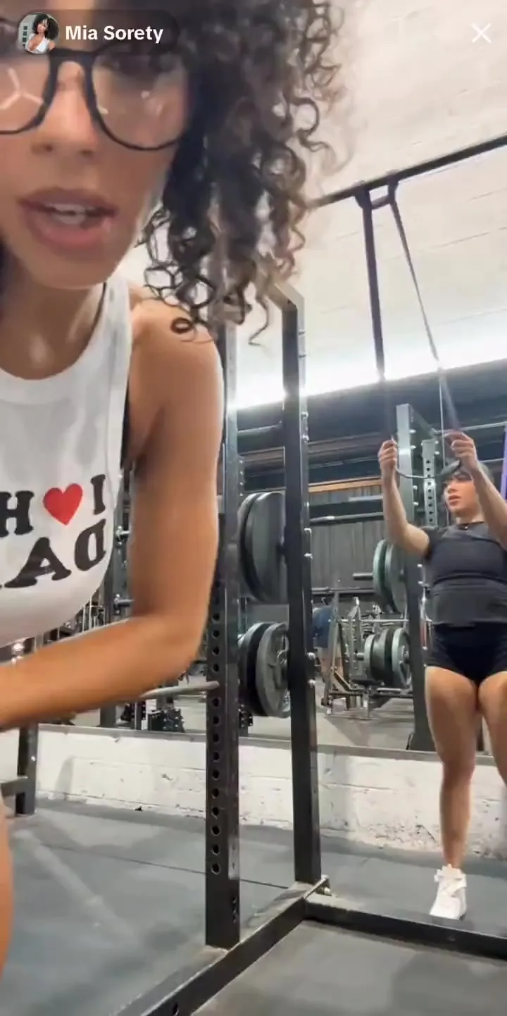 Curly-haired Miasorety works her back in red shorts, sweaty and loud, friend clowning behind her