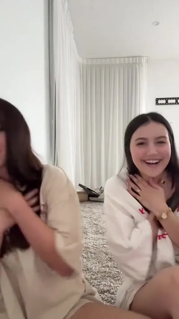Chatting and giggling on a white rug, Mikaelatesta leans in with a friend