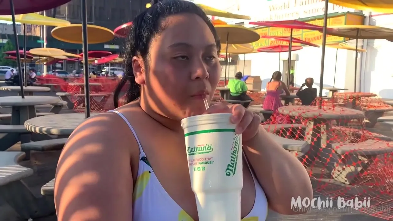 Mochiibabii licks her soft-serve cone on the sunny boardwalk, then bites into a sausage sandwich