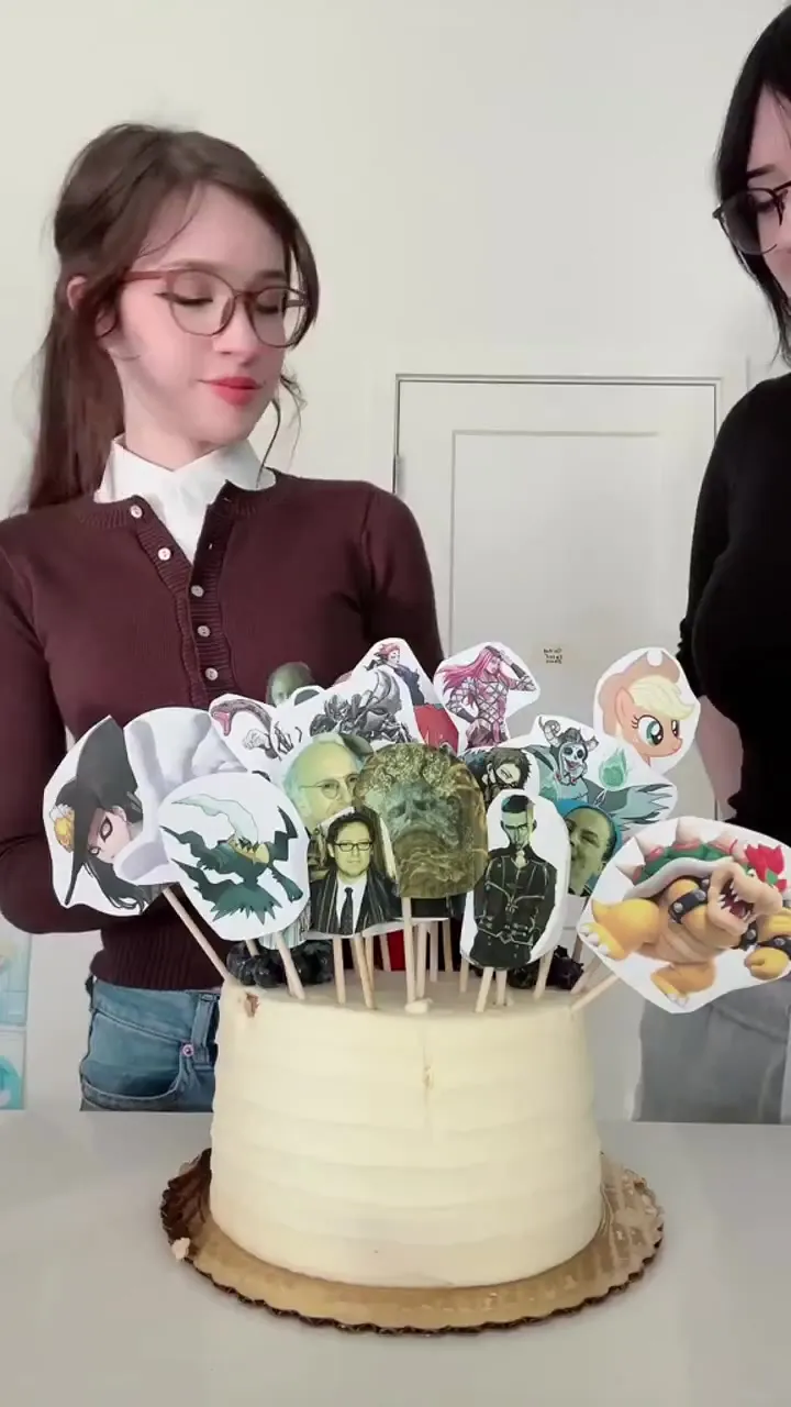 Nora Fawn frosts a cake with cartoon and celebrity toppers in a brown cardigan