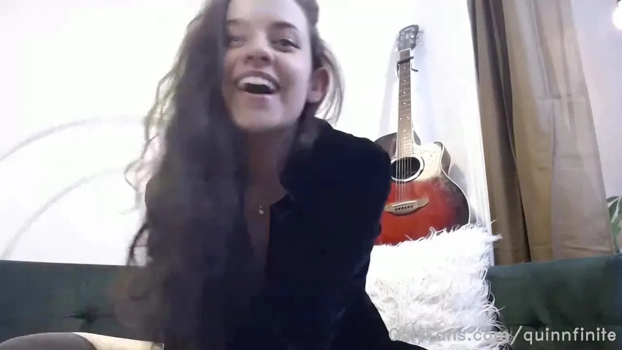 Tossing her long dark hair and laughing, Quinn Finite sprawls on the green couch in her black top