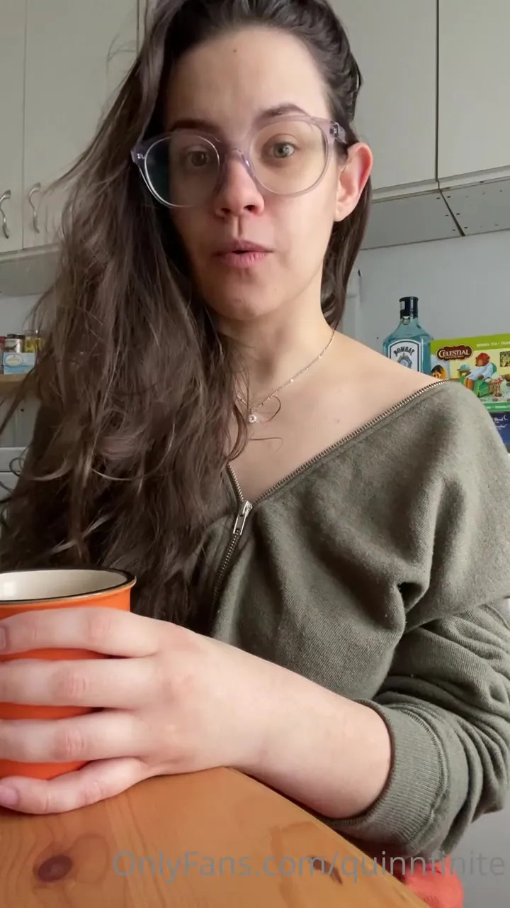 Quinn Finite sips her orange mug and grins while her zip-up slides off one shoulder