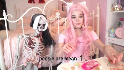Belle Delphine in pink cat ears and a pink off-shoulder top, smearing fake blood and jelly over cupcakes