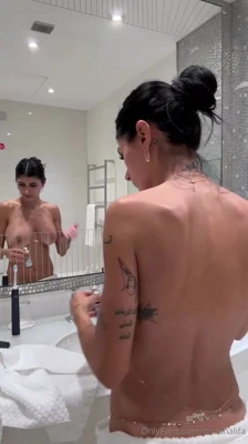 In a low white towel, Mia Khalifa brushes her teeth and lets her orange robe fall open