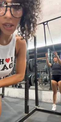 Curly-haired Miasorety works her back in red shorts, sweaty and loud, friend clowning behind her