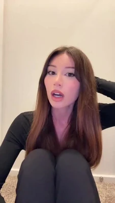 Mikaela Testa sits barefoot on the floor, red nails tapping, pleading with a needy little grin