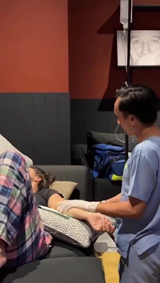 Mikaela Testa lies back with an IV drip while a man in scrubs fiddles with her arm