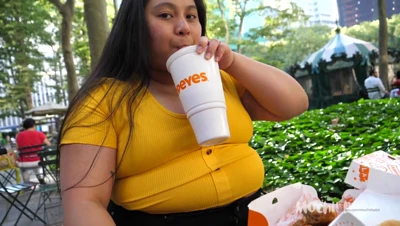 Mochiibabii digs into Popeyes chicken and mac in a yellow crop top at the park carousel