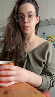 Quinn Finite sips her orange mug and grins while her zip-up slides off one shoulder