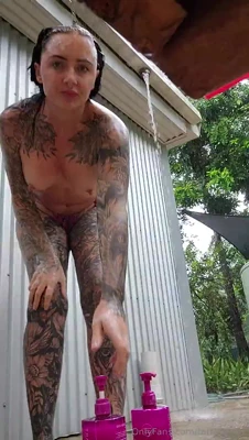 Lathering up under the outdoor shower, Muddy works her inked body and toy for a dirty finish