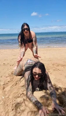 Muddy and her inked friend grapple in leopard bikinis, grinning and grinding sand
